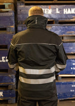 Laden Sie das Bild in den Galerie-Viewer, Hier ist eine Softshelljacke abgebildet, die winddicht und wasserabweisend ist. Eine durchdachte Taschenplatzierung ermöglicht das Tragen der Jacke im Klettergurt beim Industrieklettern in der Höhe (Ansicht hinten)
